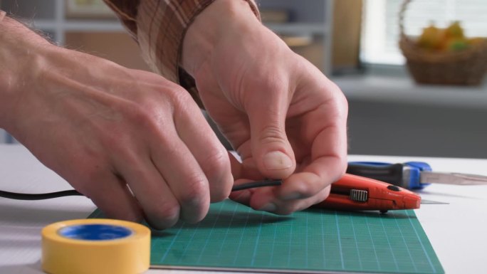 一个年轻人正在修理家里的插座，正在用一把文书刀剪家用电器插座的电线，特写
