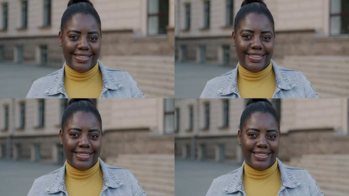在模糊的街道背景下，快乐的非裔美国女士看着相机的慢动作肖像