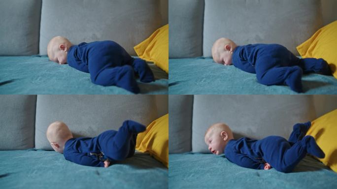穿着蓝色天鹅绒紧身衣的可爱男婴全身倒在家里的沙发上