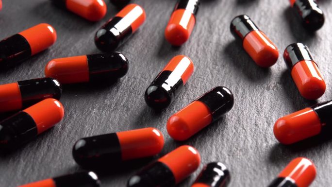 许多黑色和橙色的药丸、胶囊或抗抑郁药在黑色的盘子上在微亮的阳光下旋转。止痛头痛的药物或药物。制药行业