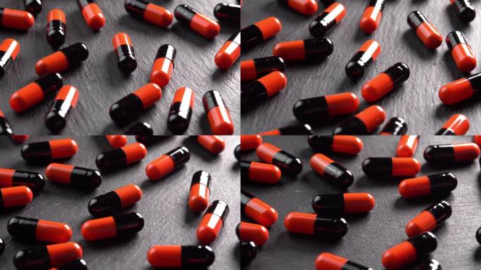 许多黑色和橙色的药丸、胶囊或抗抑郁药在黑色的盘子上在微亮的阳光下旋转。止痛头痛的药物或药物。制药行业