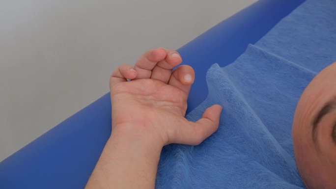 在肌肉刺激过程中，男性患者的手的特写。