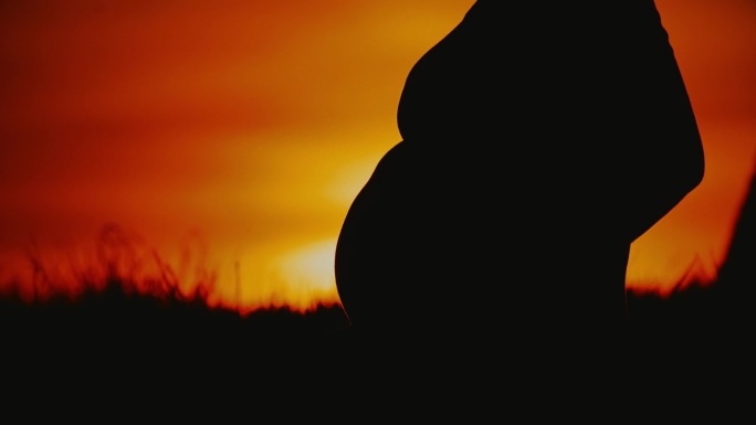 日出时，孕妇在田野里亲切地按摩腹部