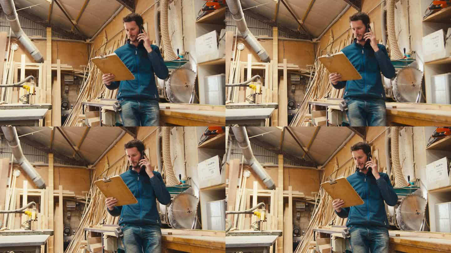 木工车间的男木匠一边看图纸一边用手机打电话