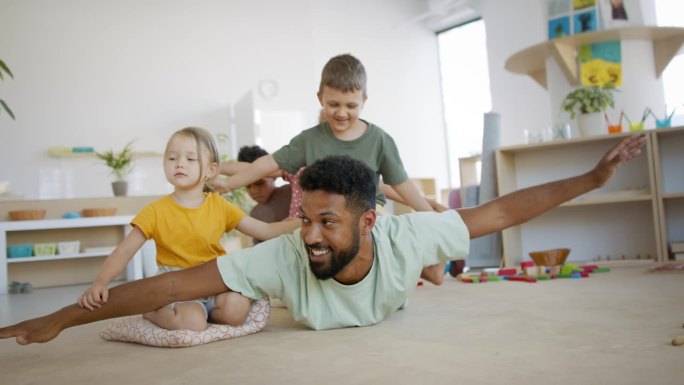 一群小幼儿园的孩子和男老师在教室里玩耍。