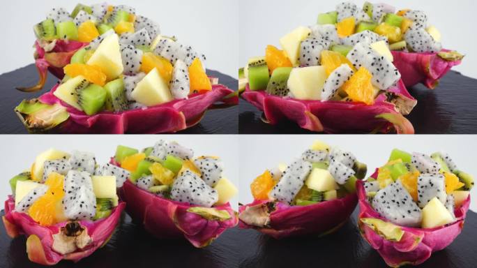 健康饮食排毒水果沙拉在皮碗的火龙果上一个黑色的石头盘子隔离在白色的背景。一片桔子、猕猴桃、苹果。