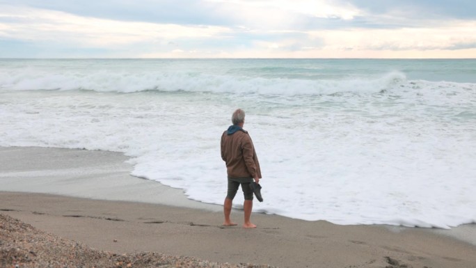 一个成熟的男人走在沙滩上，海浪很大