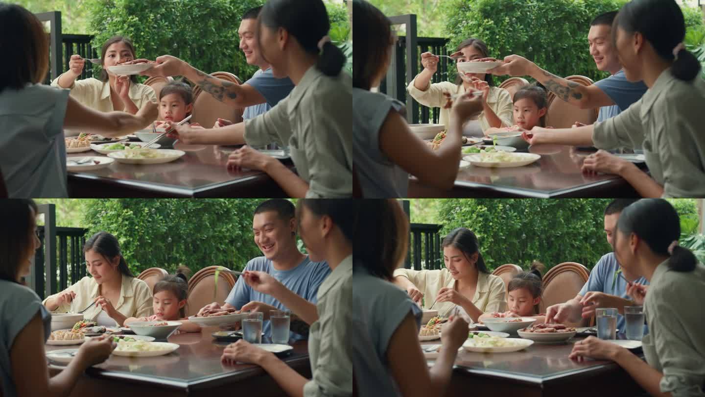 年轻的亚洲家庭吃着中国菜，坐在后院的餐桌上玩得很开心。多代同堂的家庭一起享受消费。