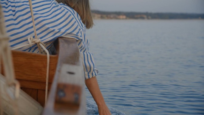 一名女子在黄昏航行时用手抚摸着水面