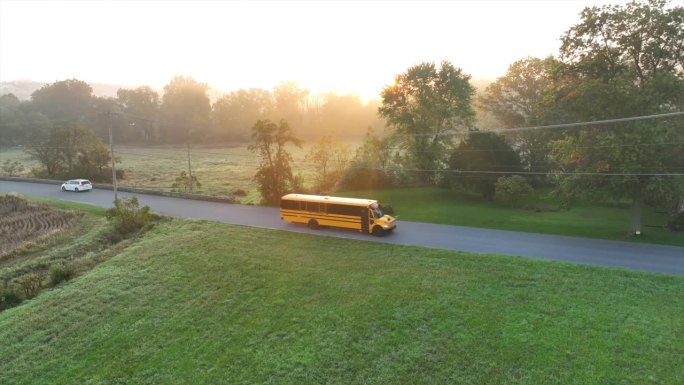 校车行驶在美国乡村的公路上。秋日朝阳中的美国教育运输。鸟瞰图。