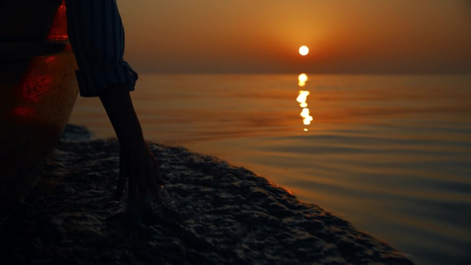 优雅的飞溅:黄昏航行时，一个女人的手抚摸着水面