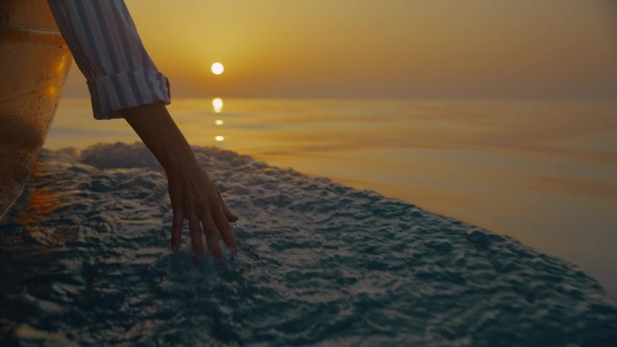 SLO莫优雅的飞溅:一个女人的手抚摸着水，而在日落航行