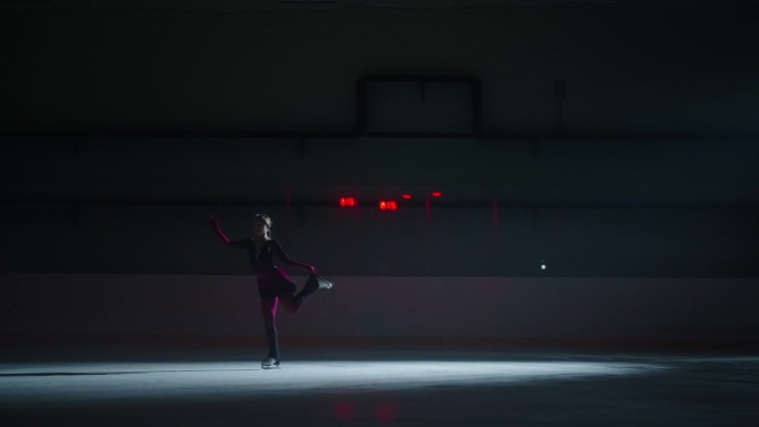 十几岁的花样滑冰女孩的剪影在溜冰场上滑冰，训练和表演技巧