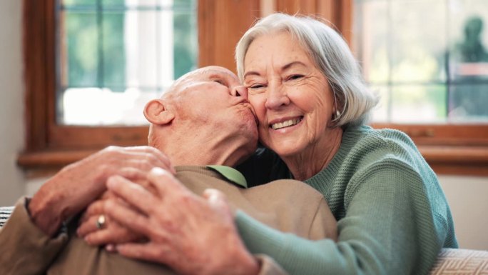在家里的沙发上和老夫妇亲亲，在客厅里快乐地依偎在一起。微笑，老年男女在休息室相爱，健康的关系和浪漫的