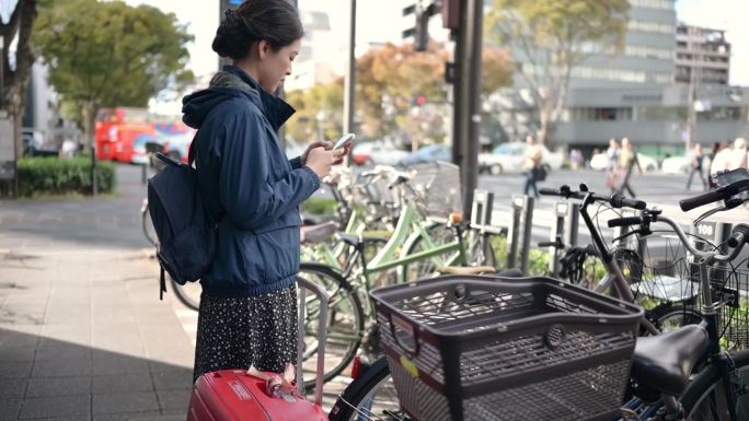亚洲游客在日本京都街头使用手机应用程序租用共享单车