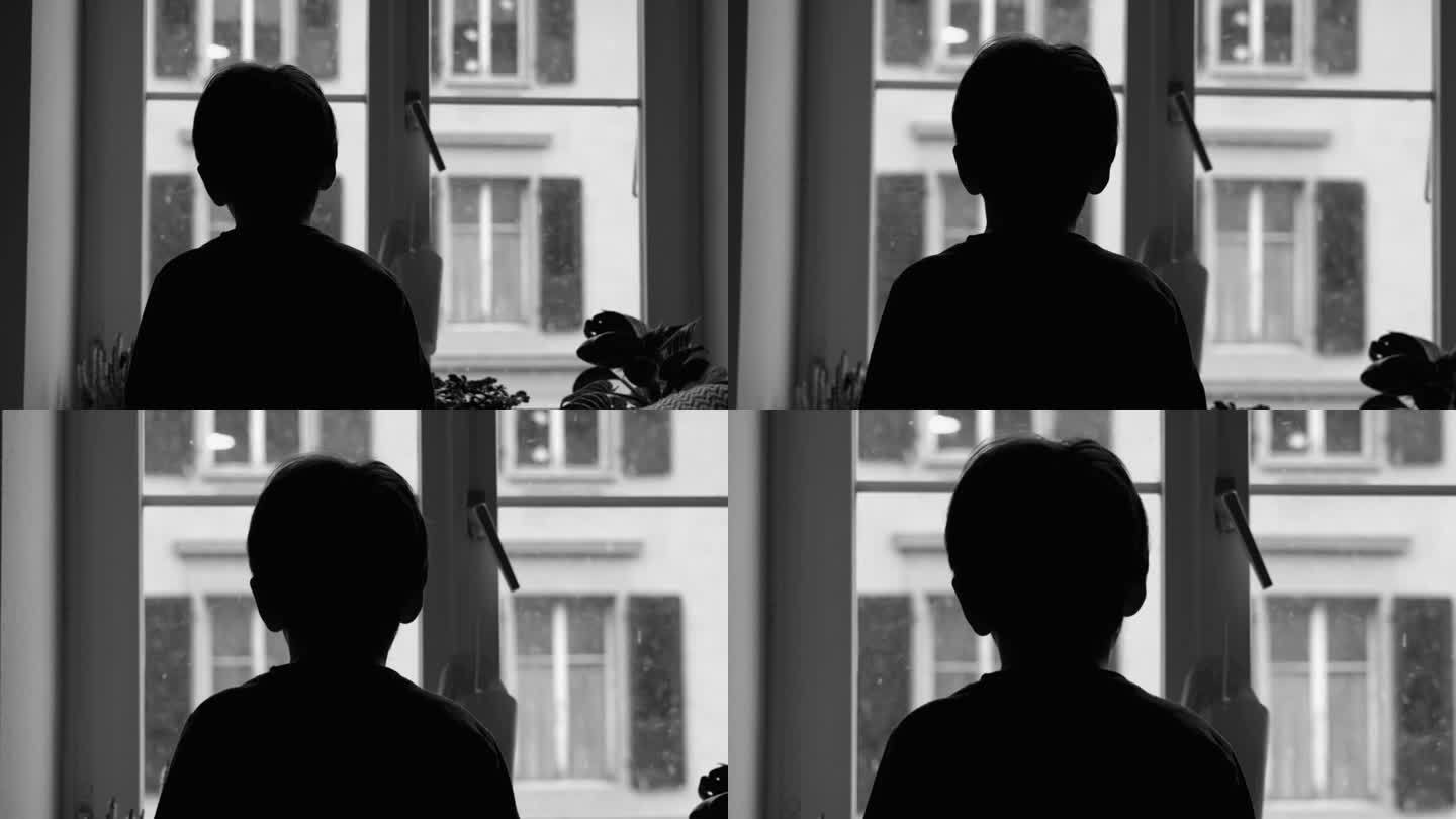 悲伤沮丧的孩子盯着公寓窗外飘落的雪花。沉思的小男孩被困在家里，在黑白单色中与抑郁症作斗争