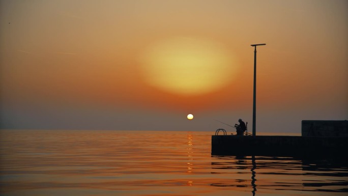 宁静的渔村:一个渔夫在码头的剪影，在夕阳下捕鱼