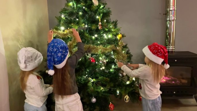 三胞胎中的三个小姐妹用玩具和花环装饰圣诞树