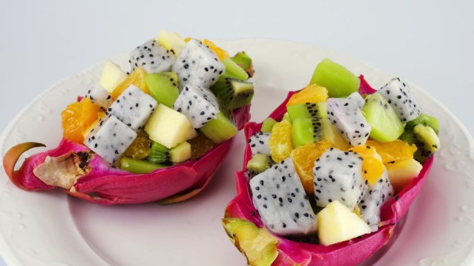 健康饮食排毒水果沙拉里的果皮碗里的火龙果放在盘子里隔离在白底上。一片桔子、猕猴桃、苹果。