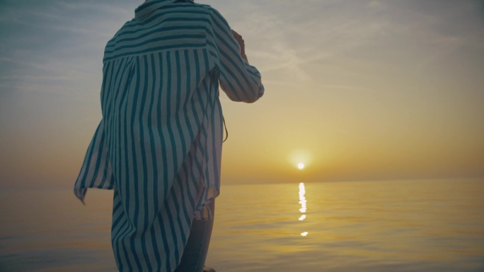 一名妇女在欣赏海上地平线上的日落时使用双筒望远镜