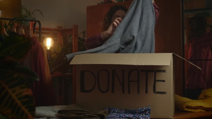 年轻的女志愿者整理衣服，把衣服放进捐款箱。
