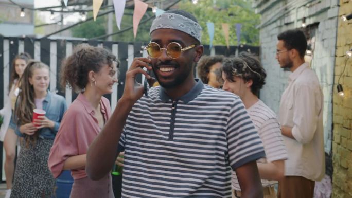 快乐的非洲裔美国人在与朋友在露天聚会上讲着手机笑着喝着酒