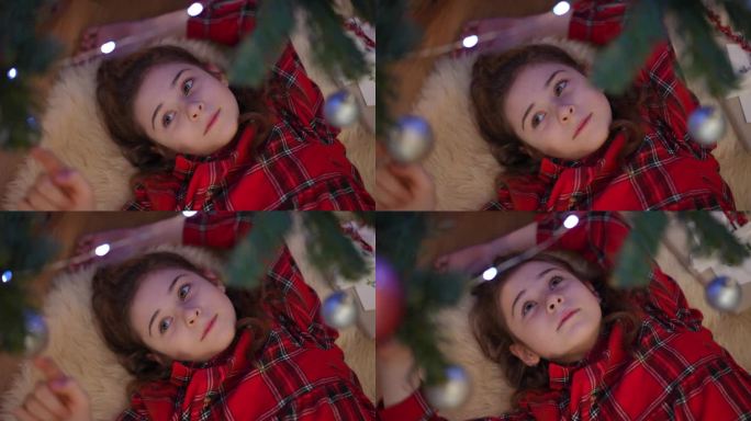 特写镜头。女孩躺在圣诞树旁，如梦似幻地玩着圣诞球。