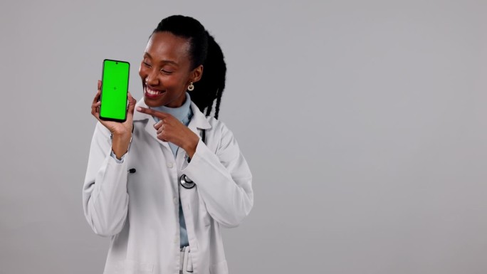 黑人女性，医生，指着一个绿屏广告手机，背景是摄影棚。非洲女性肖像或医疗保健秀移动智能手机应用程序，展