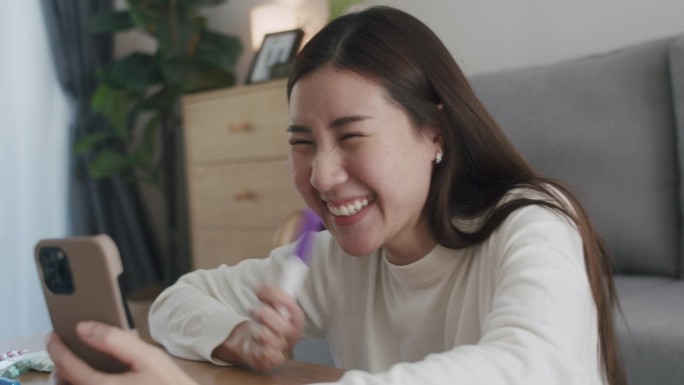 快乐的亚洲妇女在家里通过视频电话向她的丈夫展示怀孕测试呈阳性。