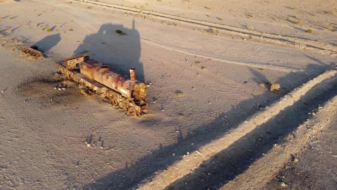 镜头慢慢地围绕着一辆孤零零的、被遗弃的、生锈的蒸汽机车，它矗立在一片沙漠之中