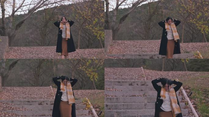 黄昏时分，一名身穿大衣、围着围巾的女子走过一座秋天的公园