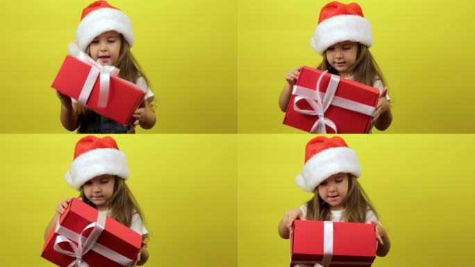 可爱的小女孩孩子戴着圣诞老人的帽子，拿着礼盒，在工作室的黄色背景墙上摆出孤立的姿势。圣诞节的概念