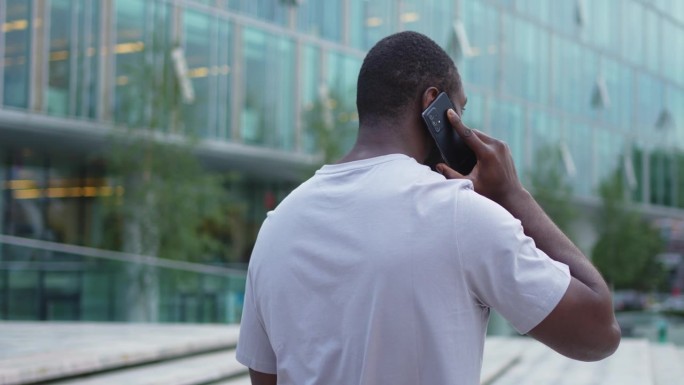一个非洲裔美国人在户外用智能手机聊天。一个不认识的人，一个拿着手机的人走在城市的街上。男人用手机接电