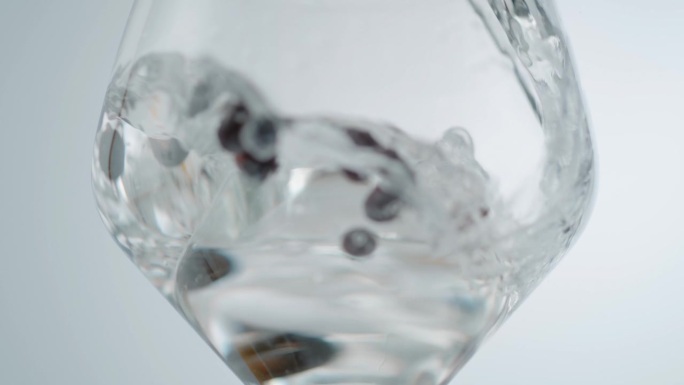 水倒在圆冰块和浆果在葡萄酒杯