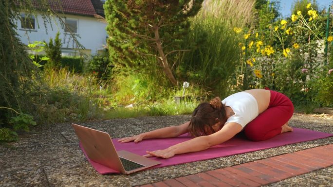 一个女人在自家后院练瑜伽，笔记本电脑上有在线教程