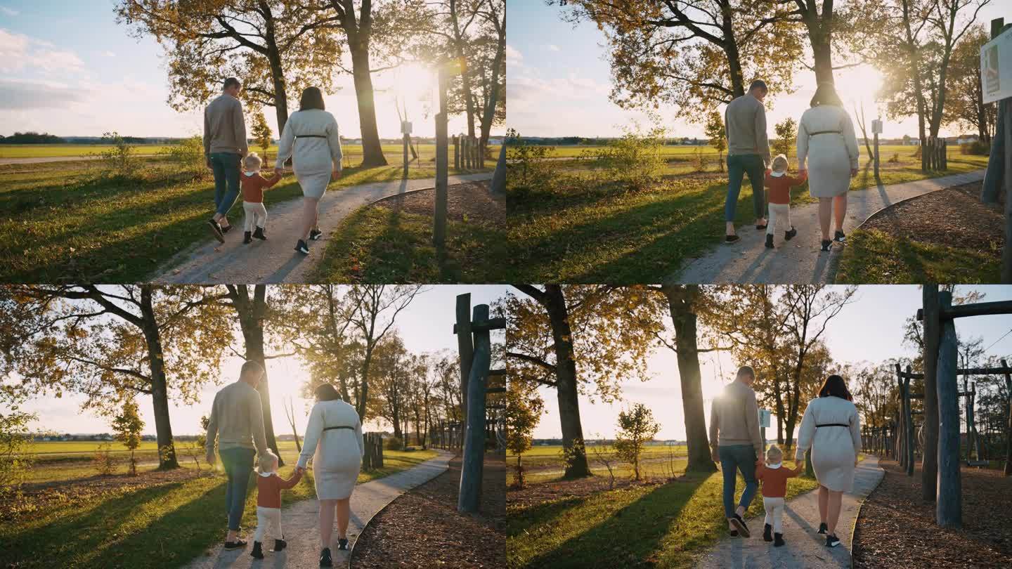 慈祥的父母牵着女儿的手走在公园人行道上的后景