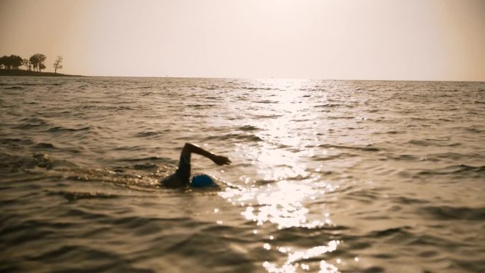 日落时，坚定的女人在广阔的海景中游泳，被锁定在天空中