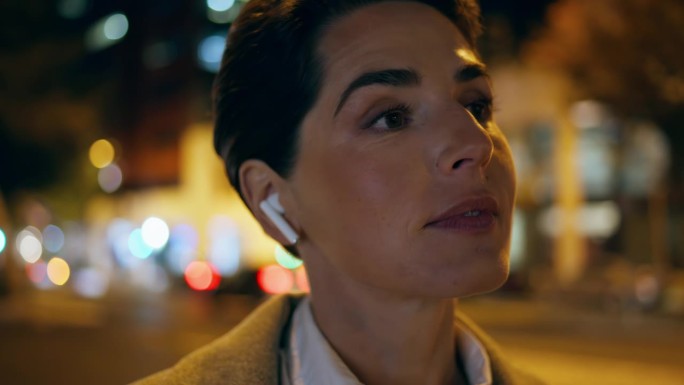 戴着耳机在夜街说话的女人特写。成功的管理者点头咨询