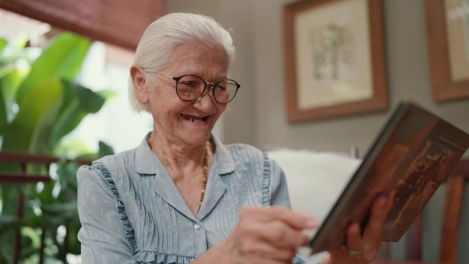 快乐的亚洲老年妇女在家里闲暇时翻阅家庭相册。年迈的祖母在看家庭照片。人生的重要时刻和记忆