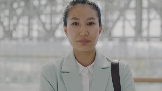 迷人的亚洲女性通勤者站在机场大厅，严肃地看着镜头