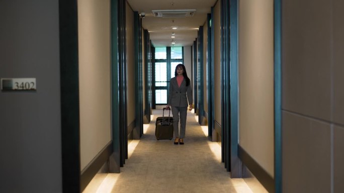 亚洲女商人提着行李箱走过酒店走廊
