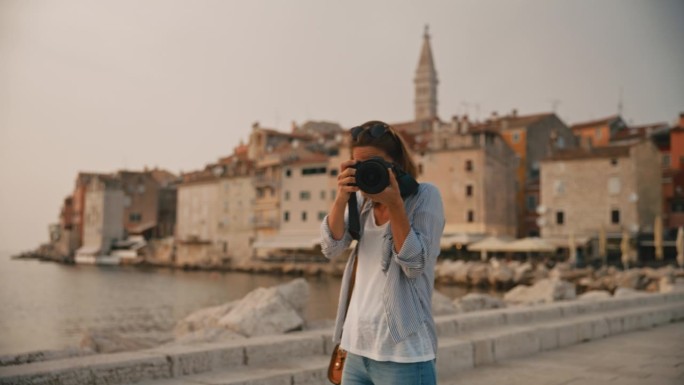 在克罗地亚度假期间，一位兴高采烈的女游客在罗维尼的老城区边看相机边拍照
