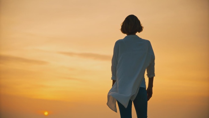 欣赏日落的女人。克罗地亚罗维尼，日落时分，女游客站在大海上广阔的橙色天空的后视图