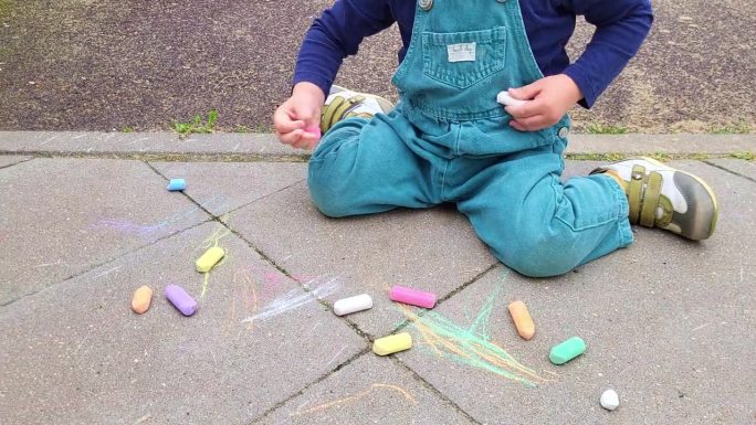 宝宝正坐在操场附近的一块瓷砖上用蜡笔画画。两岁婴儿(两岁男童)