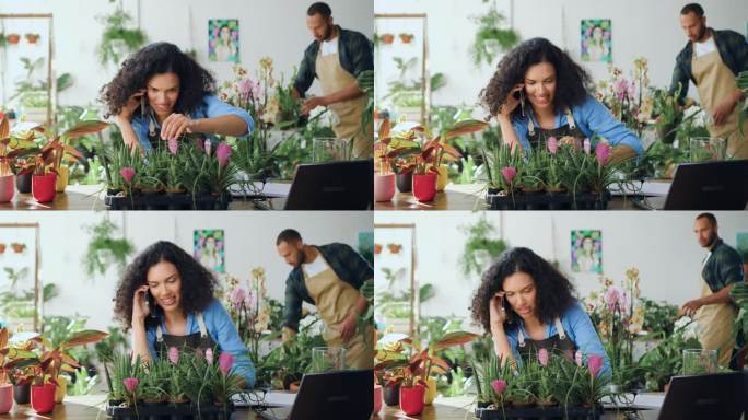 非裔美国花店女工，坐在桌边打电话，坐在舒适的花店里照顾植物。女花店老板在工作。小企业的概念。