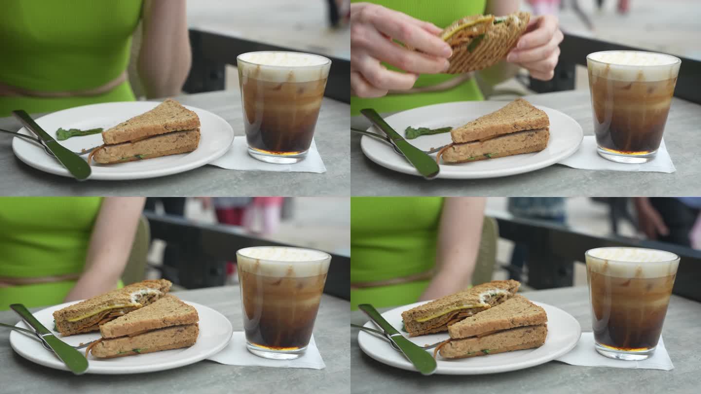 素食三明治的特写镜头。女人在外面吃三明治。冷萃咖啡加牛奶。