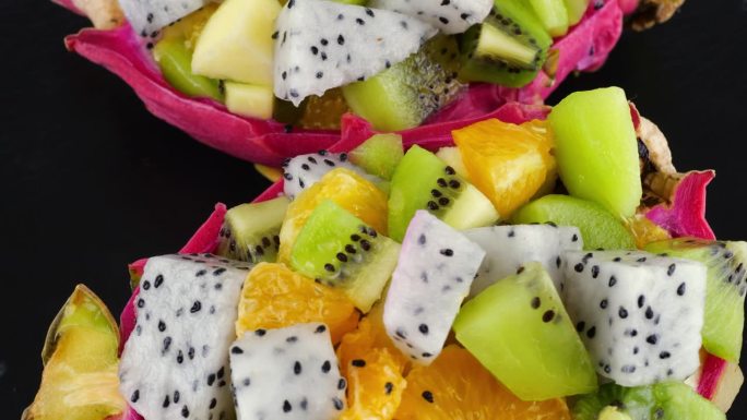 健康饮食排毒水果沙拉在皮碗的火龙果黑色石盘上。一片桔子、猕猴桃、苹果。