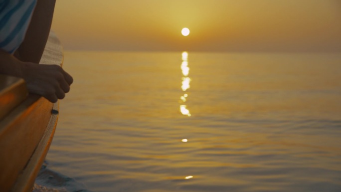 一个面目全非的女人坐在一艘帆船的船头上，欣赏着海上地平线上令人惊叹的日落