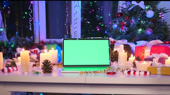 桌上放着镀铬的笔记本电脑，对面是闪闪发光的圣诞树花环，金属丝，燃烧的蜡烛