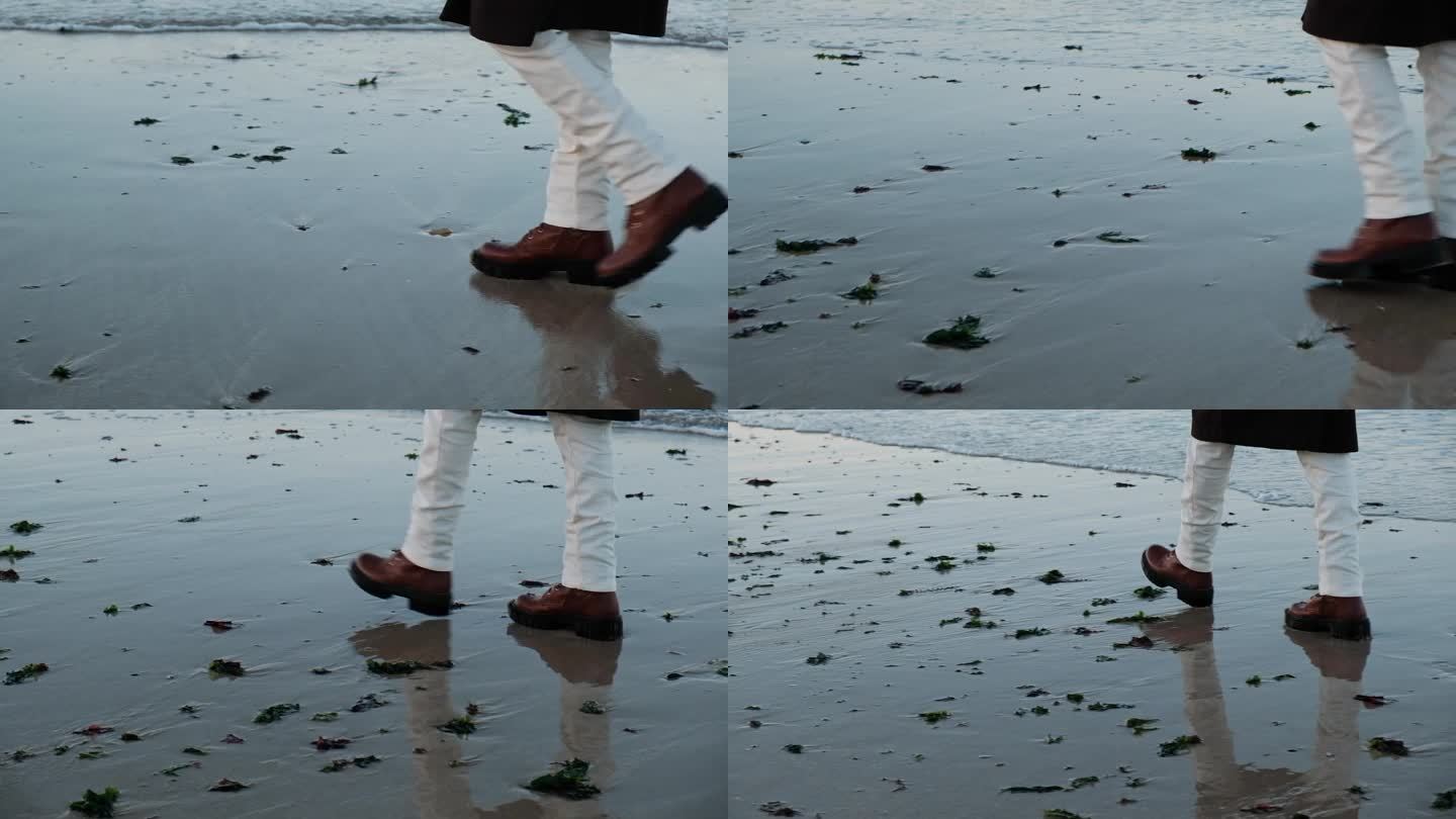 一双女性化的腿，穿着时髦的靴子，穿过潮湿的海岸，在水边潮湿的沙滩上留下精致的印记